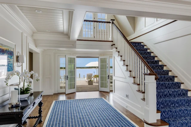 French doors in this Oyster Harbors foyer open to sweeping harbor views beyond. The space combines custom milled wall paneling, traditional balustrade, and layered moldings, grounding it in classicism while seamlessly connecting the interior to its water-facing terrace.

Architect: @patrickahearnarchitect
Photo Credit: @gregpremru