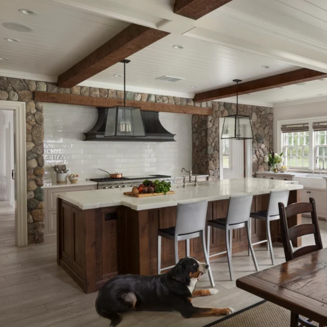In the kitchen of this Dover Colonial Revival, exposed wood beams and natural stonework lend the warmth and character of a historic New England farmhouse. A paneled ceiling, custom cabinetry, and a generous central island bring a refined sense of balance to the space.

Architecture: @patrickahearnarchitect
Builder: @sweeneycustomhomes
Photo Credit: @anthonycrisafulli